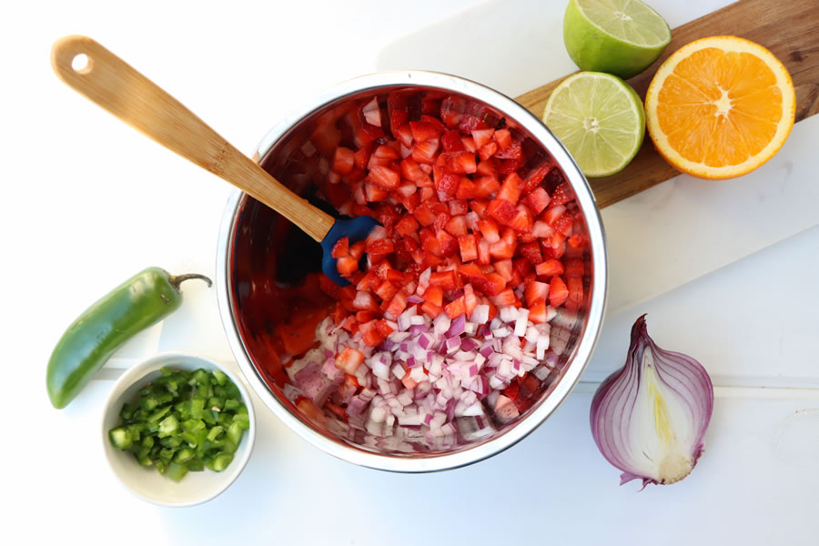 Strawberry Jalapeño Salsa ingredients being prepped. Diced strawberry and red onion in a metal bowl next to diced jalapeno, lime and onion.