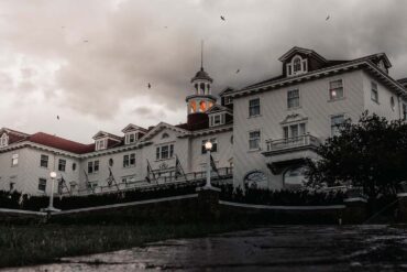 a spooky image of the haunted stanley hotel. a cloudy dusky eve with crows flying above