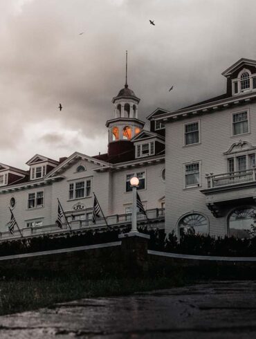 a spooky image of the haunted stanley hotel. a cloudy dusky eve with crows flying above