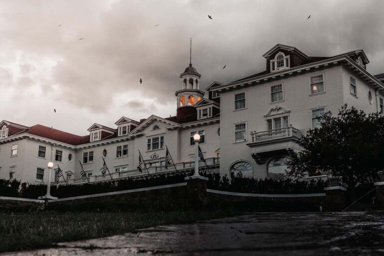 a spooky image of the haunted stanley hotel. a cloudy dusky eve with crows flying above