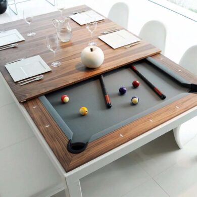 White and walnut Fusiontables dining pool table in modern dining room showing transformation from dining to pool table - wooden veneer top panels sliding to reveal gray felt playing surface with colorful billiard balls, pool cues, white contemporary chairs, wine glasses and place settings on remaining table top