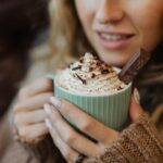 a woman drinking a homemade hot chocolate from scratch. fully decked out with topping and whipped cream.