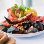 A vibrant seafood platter featuring lobster, shrimp, mussels, and lemon on a white plate.
