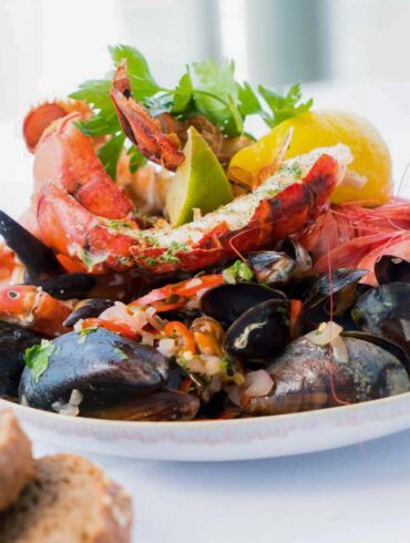 A vibrant seafood platter featuring lobster, shrimp, mussels, and lemon on a white plate.