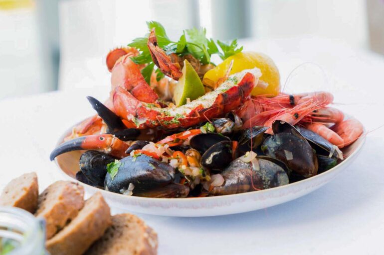 A vibrant seafood platter featuring lobster, shrimp, mussels, and lemon on a white plate.