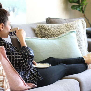 A woman drinking coffee and lounging On The Sitka Sofa From Article.com