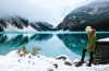 woman near crystal blue lake with mountains in the background in winter