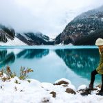 woman near crystal blue lake with mountains in the background in winter