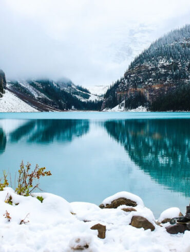 woman near crystal blue lake with mountains in the background in winter