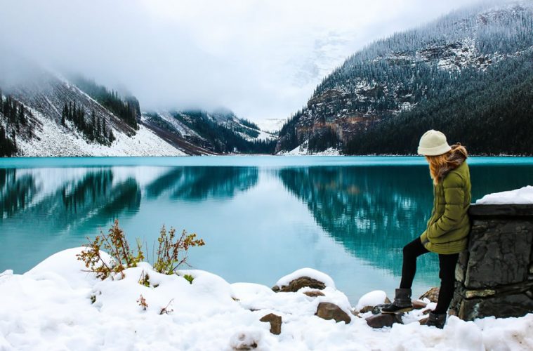 woman near crystal blue lake with mountains in the background in winter