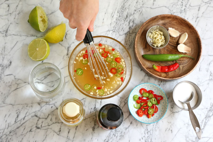 Vietnamese dipping sauce recipe being whisked in a bowl next to chilis, garlic, sugar and lime