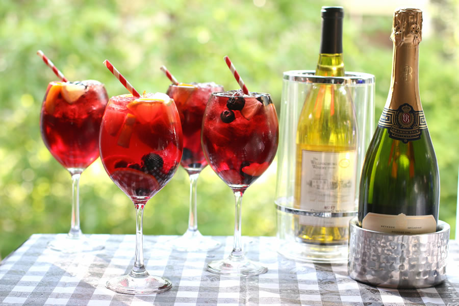 Four glasses of sangria and two bottles of champagne on an outdoor picnic table.