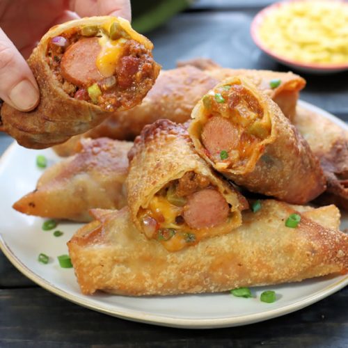 Chili Cheese Dog Egg Rolls On a Plate with a hand holding one
