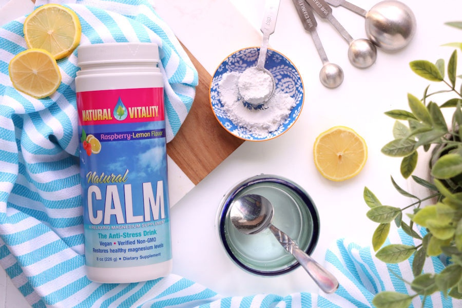 Natural Vitality Natural Calm Magnesium on a blue and white striped towel next to a glass of water lemon slices and a plant