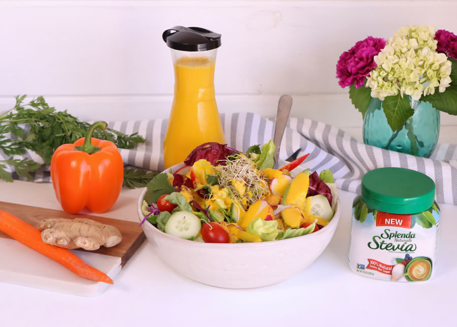 Low-Carb Carrot-Ginger Dressing Spooned over a salad next to ginger a carrot and an orange bell pepper and Splenda Stevia Naturals