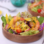 a salad with carrot ginger dressing spooned over it with shrimp