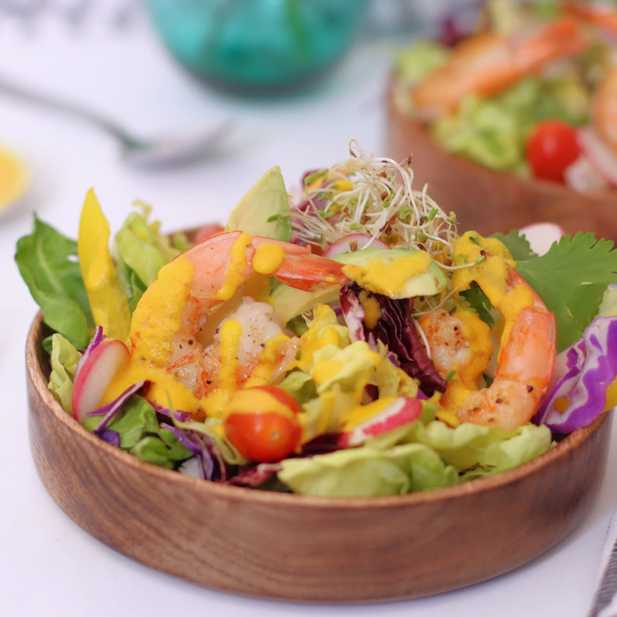 a salad with carrot ginger dressing spooned over it with shrimp