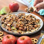 a hand holding up an apple slice with chocolate sauce peanut butter coconut peanuts and FitJoy protein bar crumble