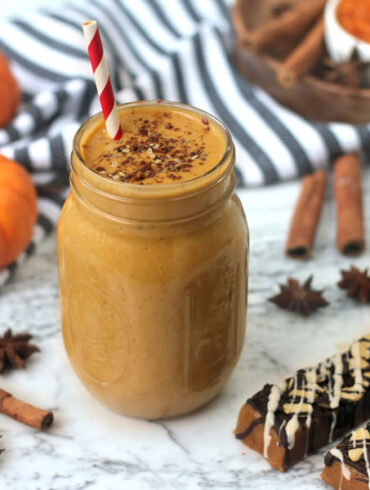 pumpkin pie protein shake in a mason jar next to pumpkin protein bar on marble next to mini pumpkins