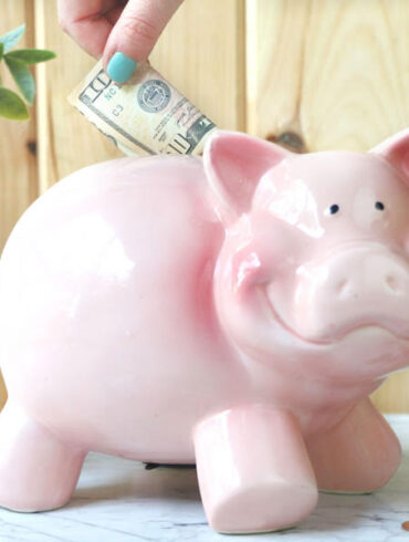 putting money in a pink piggy bank https://www.onbetterliving.com