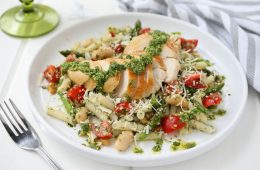 A plate of Gluten -Free Chicken Basil Pesto Pasta with a fork, gray and white striped napkin
