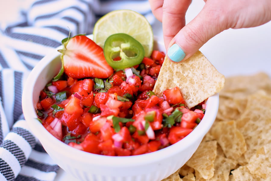 Einen Tortillachip in die Erdbeer-Jalapeño-Salsa in einer weißen Schüssel tauchen