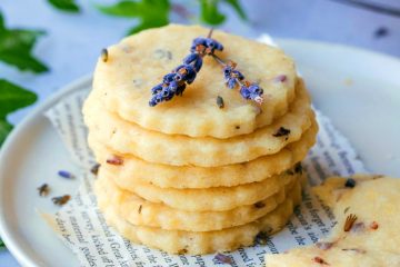 a stack of 6 buttery lavender shortbread cookies on a plate with lavender sprigs