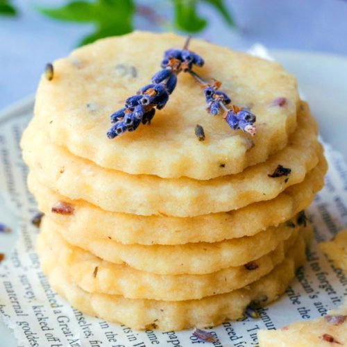 a stack of 6 buttery lavender shortbread cookies on a plate with lavender sprigs