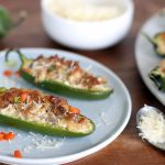 2 baked jalapenos with sausage, cream cheese, asiago and parmesan cheese on a plate