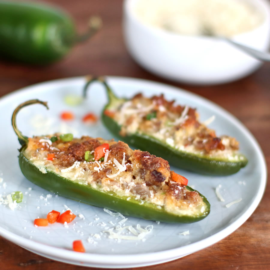2 baked jalapenos on a plate with sausage and asiago cheese