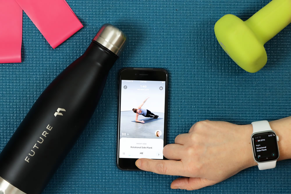 Using the Future fitness app for a workout on a yoga mat with a water bottle, bands, and a dumbbell
