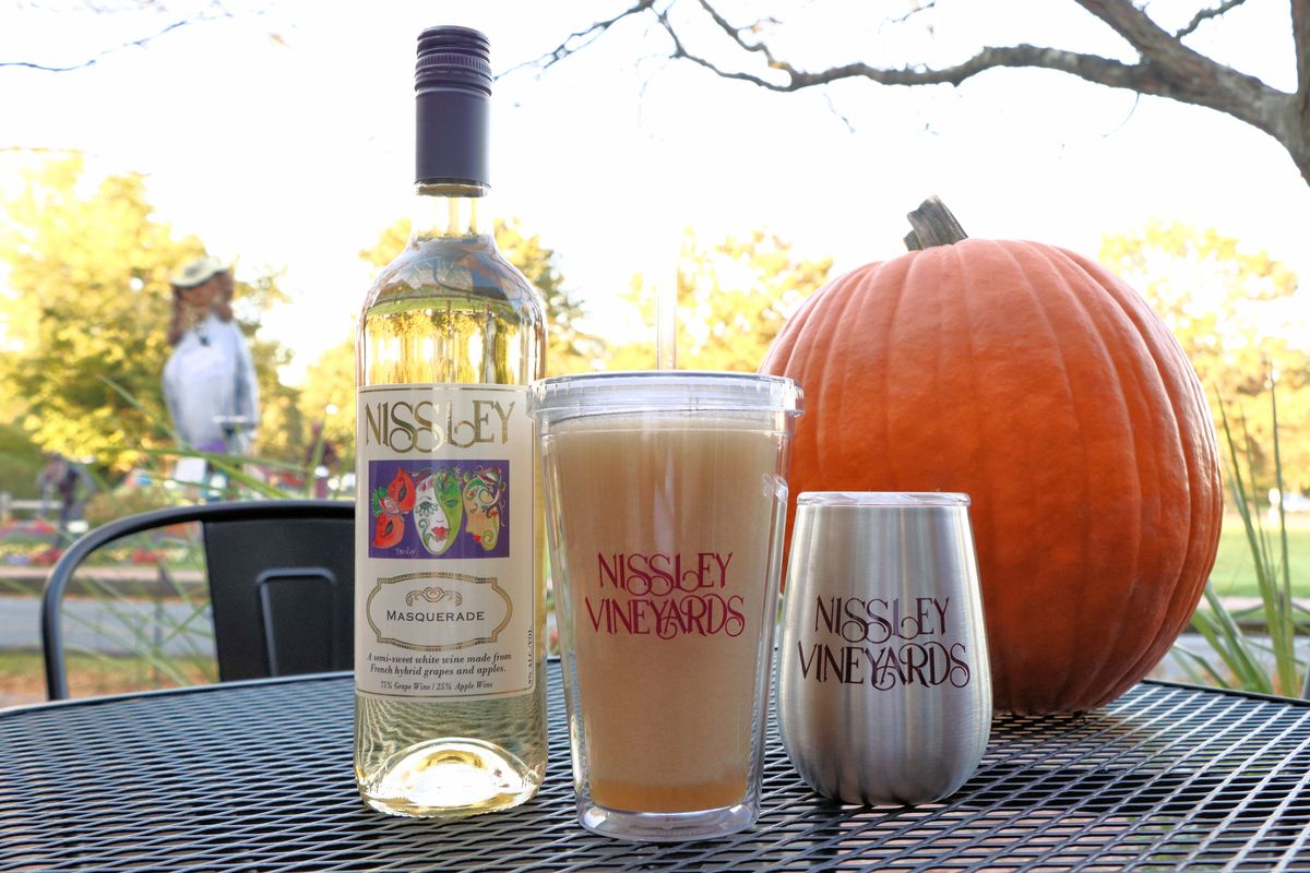 An apple wine slushie, a bottle of wine, a pumpkin, and a tumbler of wine on the outdoor patio of Nissley Vineyards at Peddlers Village