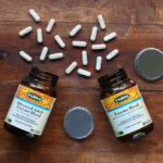 Advanced Adult Enzyme Blend and Enzyme Blend from Flora on a wooden table with capsules out.