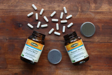 Advanced Adult Enzyme Blend and Enzyme Blend from Flora on a wooden table with capsules out.