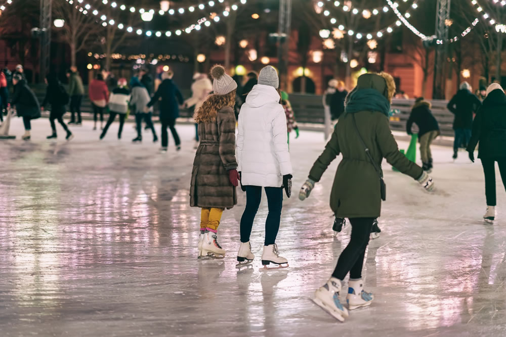 A group of women are ice skating in an outdoor rink in the winter time. 