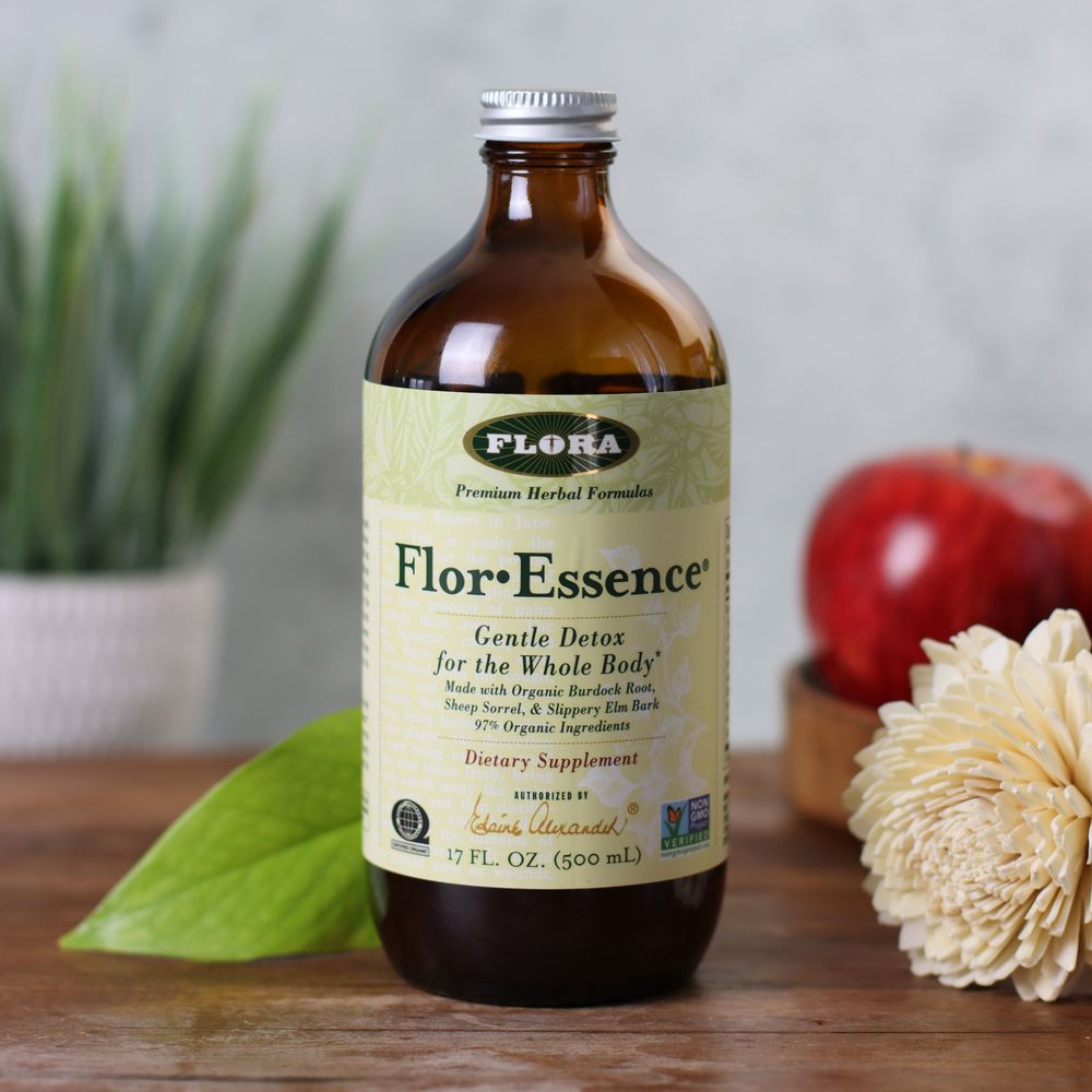 A bottle of Flor-Essence on a table next to a flower, plant, and apple.
