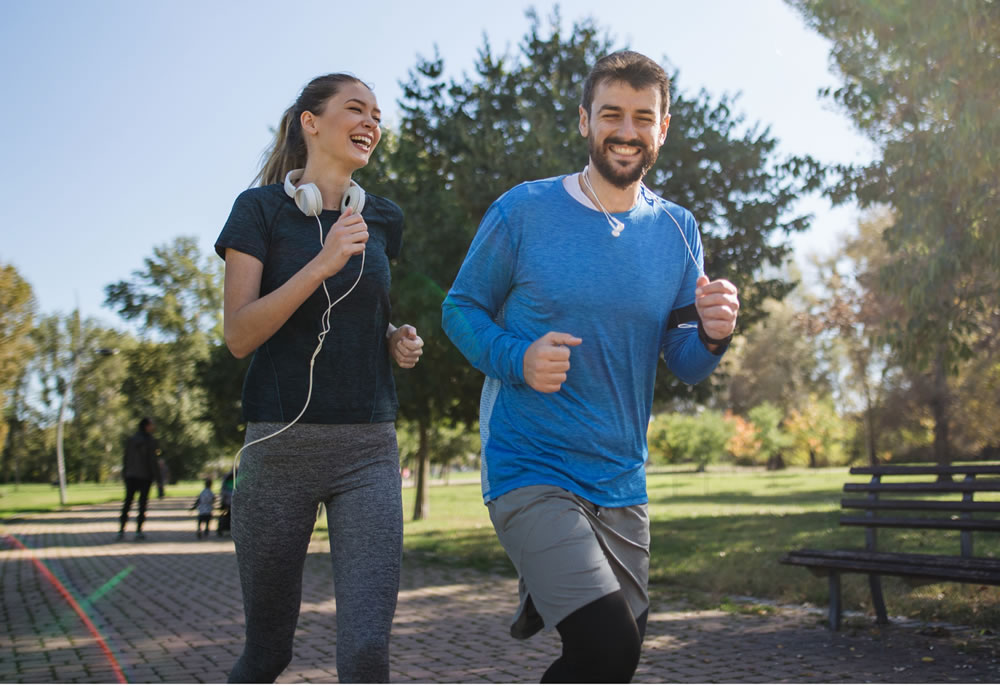 A man and woman are having fun jogging together in a park like setting.