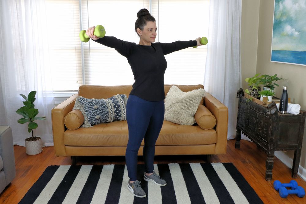 A woman working out at home with a pair of dumbbells in her living room.