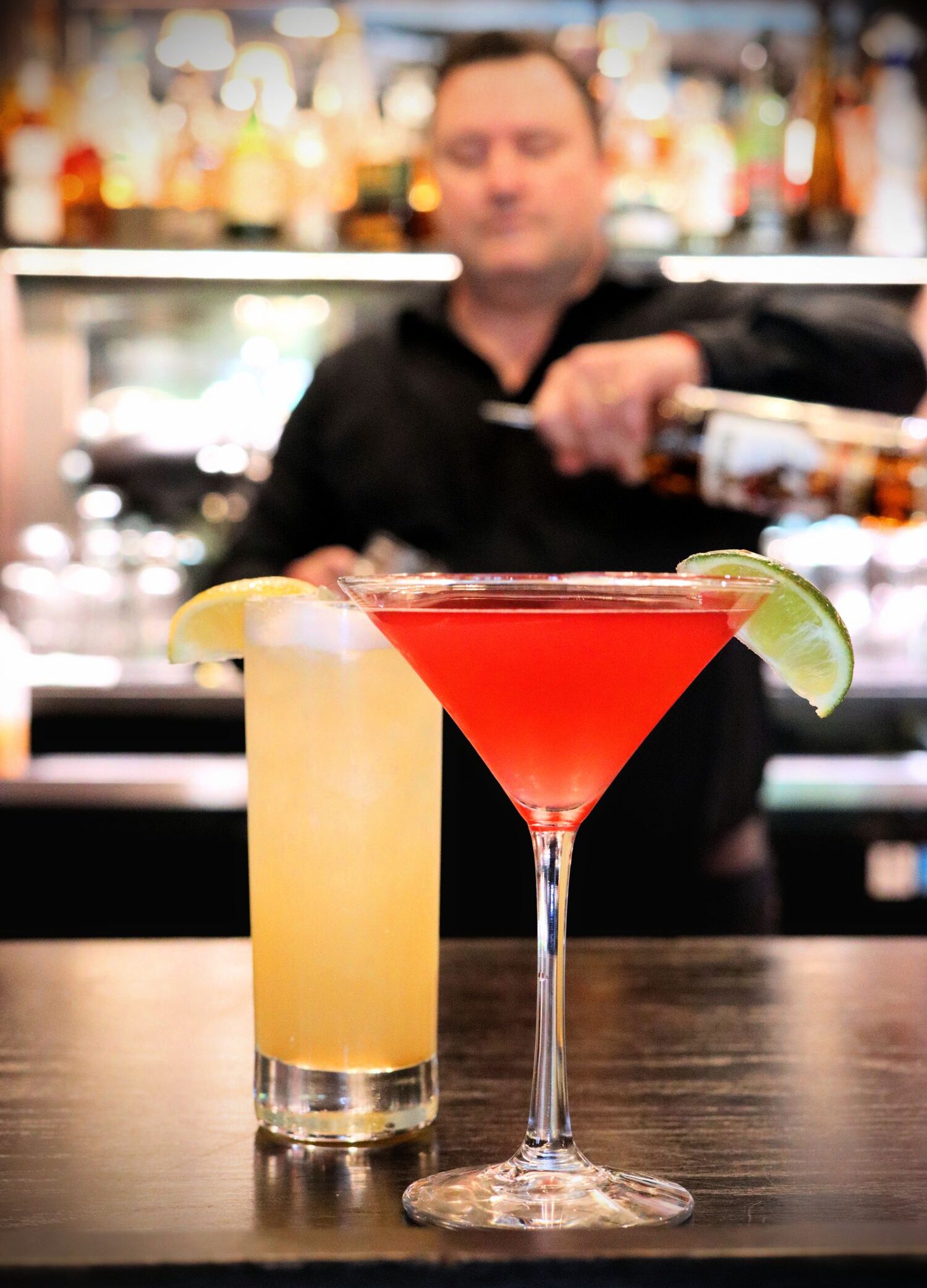Cocktails at Red Fox Lounge. A bartender is pouring in the background. Two colorful cocktails in the foreground.