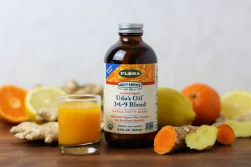 A ginger turmeric wellness immune shot with a bottle of udos oil surrounded by ingredients
