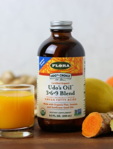 A ginger turmeric wellness immune shot with a bottle of udos oil surrounded by ingredients
