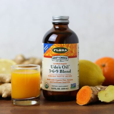 A ginger turmeric wellness immune shot with a bottle of udos oil surrounded by ingredients