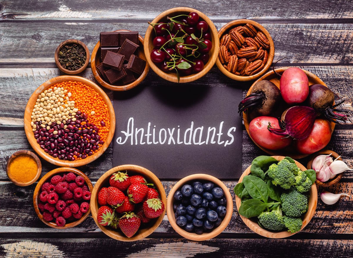A selection of bitter antioxidant foods in bowls, including onion, broccoli, cocoa, and more