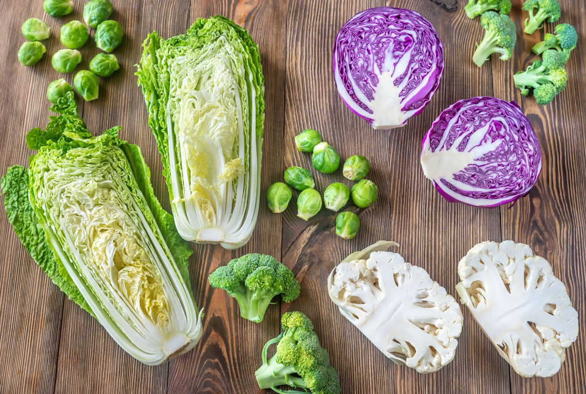 A selection of bitter foods on a chopping block, including brussels spouts, cabbage, broccoli, and cauliflower