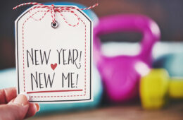 A person holding a New Year, New Me sign in front of a weight set.