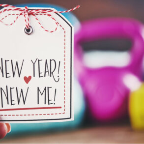 A person holding a New Year, New Me sign in front of a weight set.