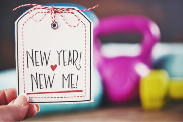 A person holding a New Year, New Me sign in front of a weight set.