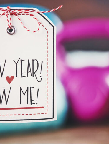 A person holding a New Year, New Me sign in front of a weight set.