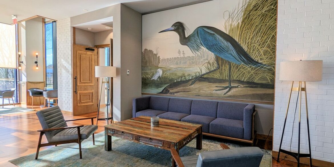 A sitting area to relax at The Rookery at the Merriweather Lakehouse Hotel in Columbia Maryland. A couch, table, two chairs, and a wall mural of a heron.