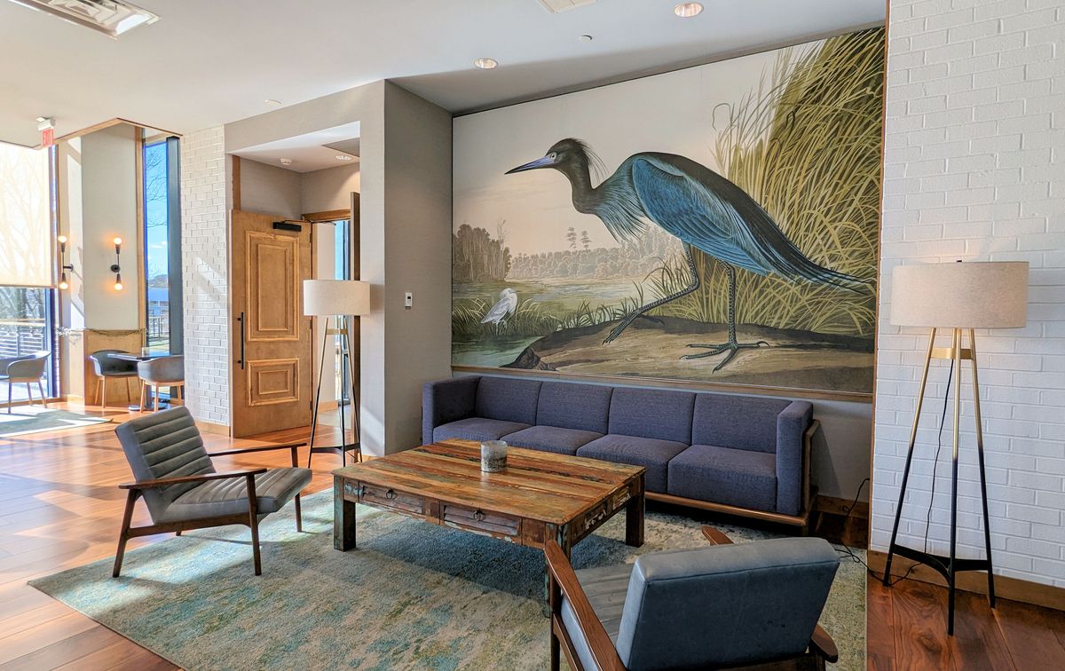 A sitting area to relax at The Rookery at the Merriweather Lakehouse Hotel in Columbia Maryland. A couch, table, two chairs, and a wall mural of a heron.